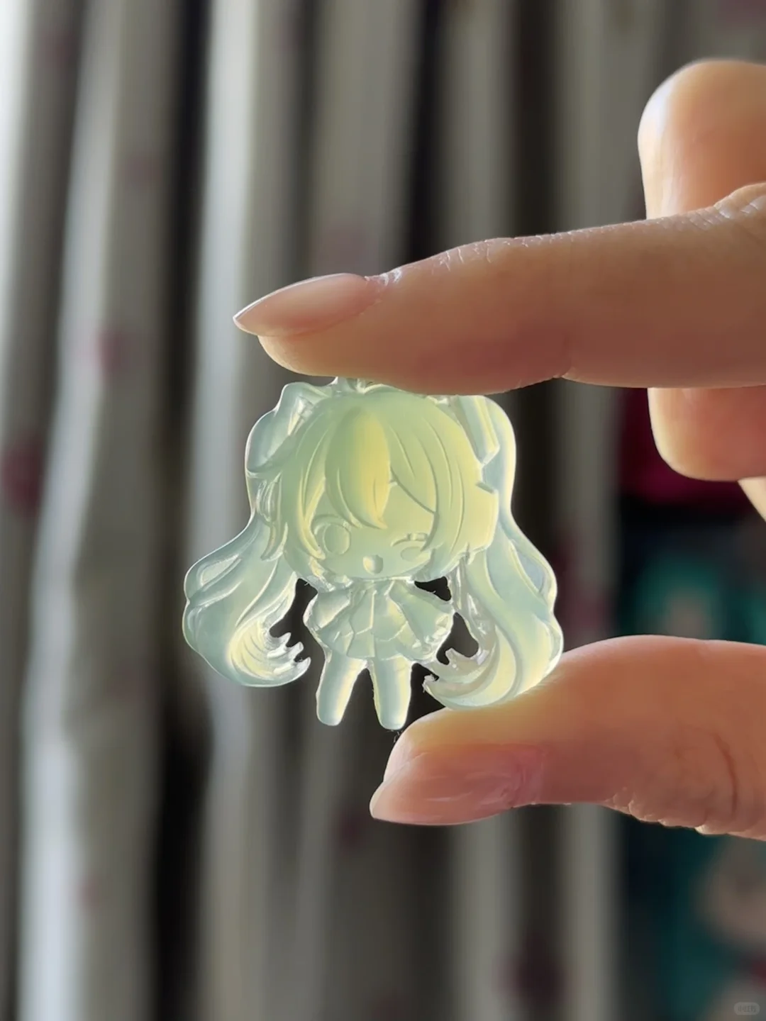 Hatsune Miku pendant 3A46 held between two fingers, with light shining through the winking figure and twin tails